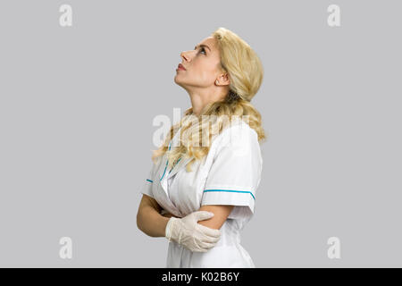 Portrait de la pensée infirmière. Belle jeune femme médecin ou infirmière de penser et à la recherche sur fond gris, vue de côté. Banque D'Images