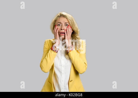 Portrait de jeune femme horrifiée. Desperate young blonde woman touching her face à la confusion et terrifié, fond gris. Banque D'Images