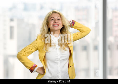 Cheveux blonds Dame posant à l'appareil photo. Cheeerful European young woman holding hands dans les cheveux sur fond flou. Banque D'Images