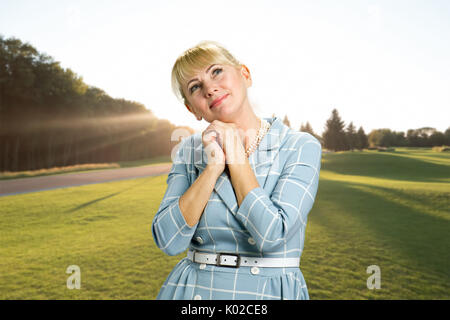 Portrait of smiling woman. Femme d'âge moyen joignit ses mains sous le menton et à la pensée vers le haut et souriant sur fond nature. Banque D'Images