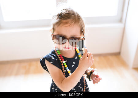 Jolie petite fille en robe et big Sunglasses at home. Banque D'Images