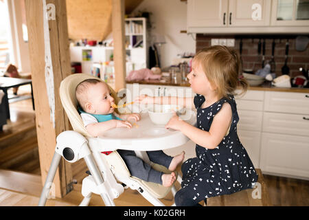 Cute little girl at home nourrir son petit frère. Banque D'Images