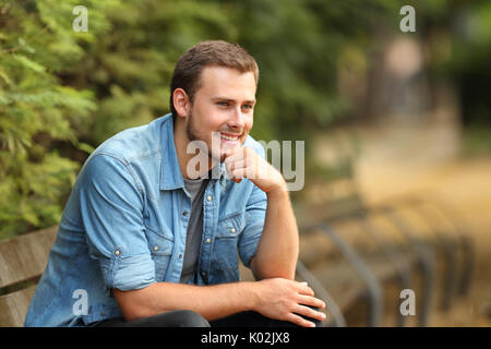 Portrait of a smiling guy looking away assis sur un banc dans un parc Banque D'Images