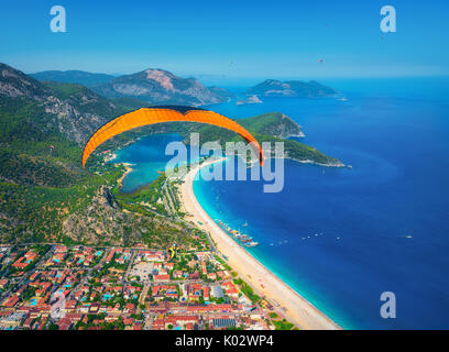 Parachute dans le ciel. Tandem parapente voler au-dessus de la mer avec de l'eau bleue et les montagnes en journée ensoleillée. Vue aérienne de la bleue et de parapente Banque D'Images