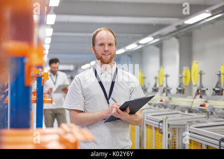 Portrait souriant, confiant surveillant masculin avec presse-papiers à l'usine de fibre optique Banque D'Images