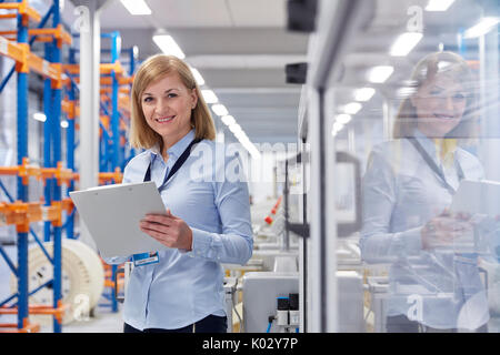 Portrait of smiling female superviseur avec presse-papiers à l'usine de fibre optique Banque D'Images