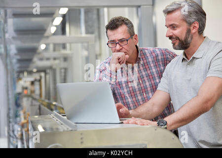 Les surveillants masculins using laptop in factory Banque D'Images