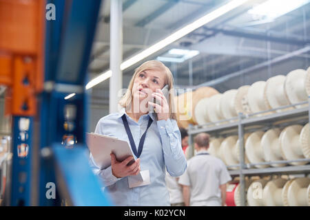 Femme comme superviseur avec presse-papiers talking on cell phone in la fibre optique factory Banque D'Images