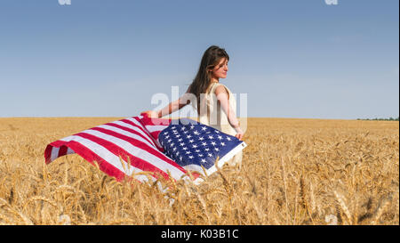 Belle fille brune en robe de lin naturel avec un drapeau américain dans le domaine Banque D'Images