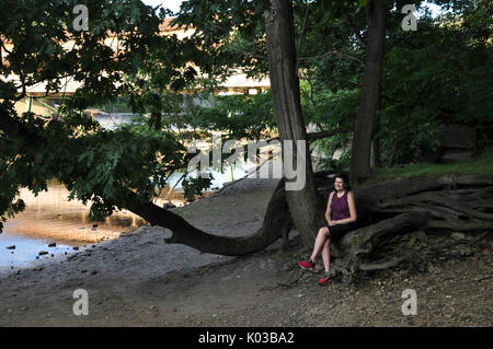 Femme assise sous un arbre d'ombrage sur les rives de la rivière Grand au Harpersfield Covered Bridge Metro Park dans Ashtabula Comté (Ohio). Banque D'Images