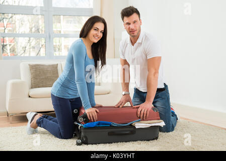 Portrait of Young Smiling Couple essayant de fermer Valise avec beaucoup de vêtements Banque D'Images