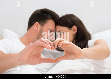 Couple Lying On Bed formant avec la main en forme de coeur Banque D'Images