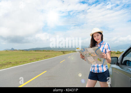 Belle hat woman holding paper site trouver le bon itinéraire touristique debout à côté d'un voyage personnel voiture avec sunny route asphaltée, arrière-plan. Banque D'Images