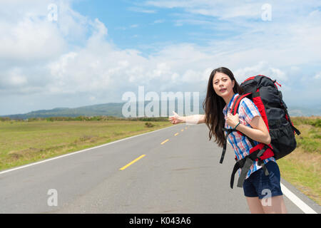 Female traveler standing on road décisions thumb up geste pour l'auto-stop en espérant trouver sa voiture passant à la station de transfert quand elle en Banque D'Images