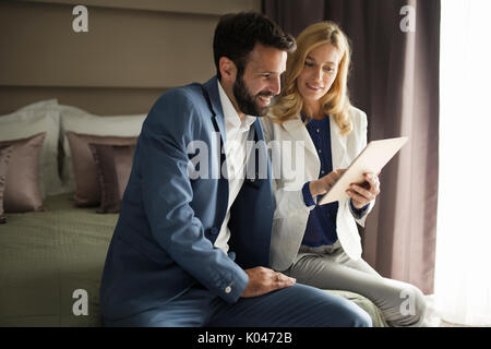 Businessman and businesswoman sitting on bed and using tablet Banque D'Images