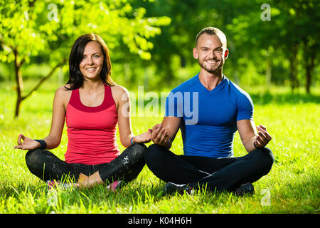 Young man and woman doing yoga dans le parc d'été ensoleillé Banque D'Images