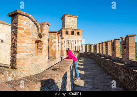 Vigoleno, Piacenza, Italie, Emiglia-Romagna. Femme debout sur les murs du château à la ville ci-dessous. Banque D'Images