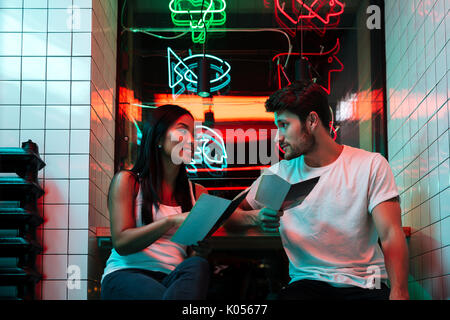 Photo de jeunes heureux multiethnique loving couple sitting in Cafe à côté holding menu du restaurant. Banque D'Images