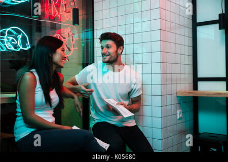 Image of smiling couple aimant multiethnique assis dans un café à côté du restaurant holding. Banque D'Images