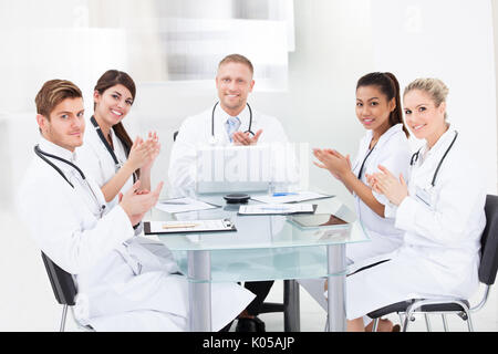 Portrait of confident doctors applaudir alors que sitting at desk in clinic Banque D'Images