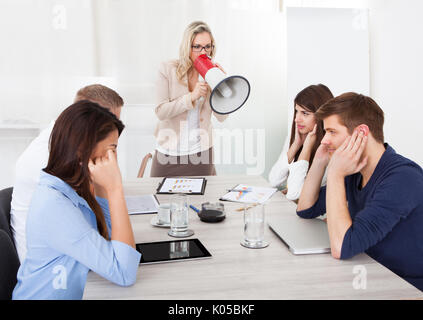 Angry businesswoman crier par mégaphone sur les collègues de bureau à la réunion Banque D'Images