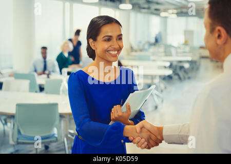 Smiling businesswoman shaking hands with businessman in office Banque D'Images