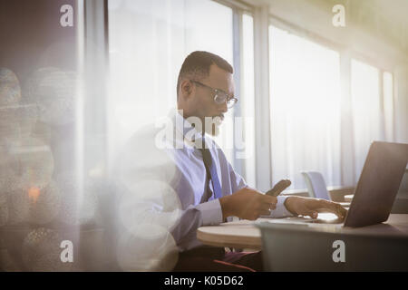 De graves businessman texting with cell phone at laptop in office Banque D'Images