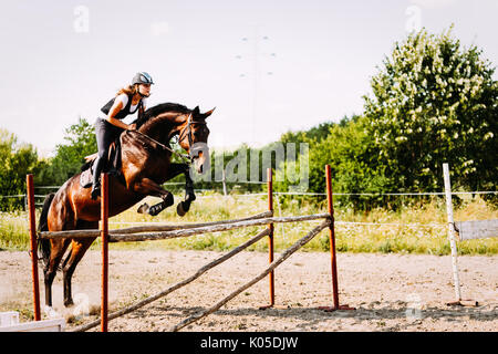 Jeune femme jockey à Cheval sautant par-dessus obstacle Banque D'Images