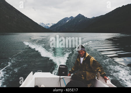 Un homme entraîne un moteur bateau naviguant dans la soirée sur un lac de montagne sur fond de belles montagnes enneigées. 28 juin 2017 Banque D'Images