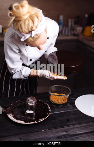 Glaze un gâteau au chocolat. Le confiseur est une jeune femme, glaçures un gâteau et garnitures avec l'or. Banque D'Images