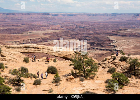 Les touristes à pied à travers le désert broussailleux protégé du soleil par des parasols à l'île dans le ciel, terres Canyon National Park Utah, USA. Banque D'Images