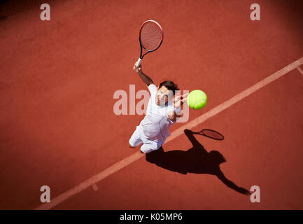 Vue aérienne du jeune joueur de tennis masculin en jouant au tennis, au service de la balle de tennis au soleil