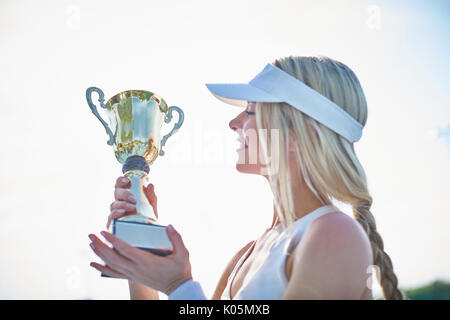 Jeune femme blonde en joueur de tennis visor holding trophée du championnat Banque D'Images