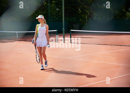 Les jeunes tennis player marche avec raquette de tennis sur terre battue de soleil Banque D'Images
