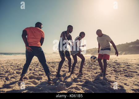 Jeunes amis jouant au football sur la plage de sable. Les peuples africains bénéficiant d'un match de football sur la journée d'été. Banque D'Images