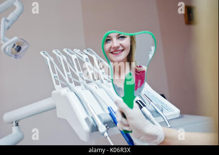 Belle dentiste montrant ses nouvelles dents du patient par le miroir dentaire en cabinet. Banque D'Images