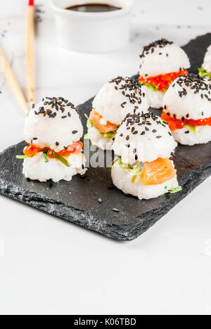 L'alimentation hybride de tendance. Japanese cuisine asiatique. Sushi Mini-hamburgers, sandwiches au saumon, wakame hayashi, daikon, gingembre, caviar rouge. Table en marbre blanc, Banque D'Images