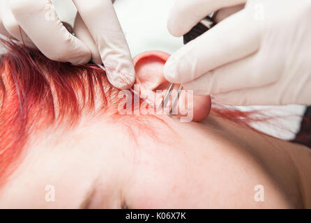 Professionnels Piercing poussant la canule à travers la peau pendant qu'il s'est emparée de l'oreille. Type tragus Banque D'Images