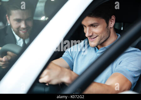 Young smiling couple test d'une nouvelle voiture alors qu'il était assis à l'intérieur avec un concessionnaire Banque D'Images