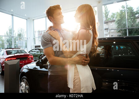 Happy young couple hugging après l'achat d'une nouvelle voiture chez le concessionnaire Banque D'Images