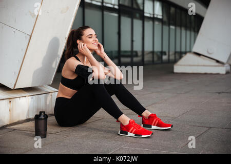 Photo de sport magnifique jeune femme assise avec vos écouteurs à l'extérieur et à côté. Banque D'Images