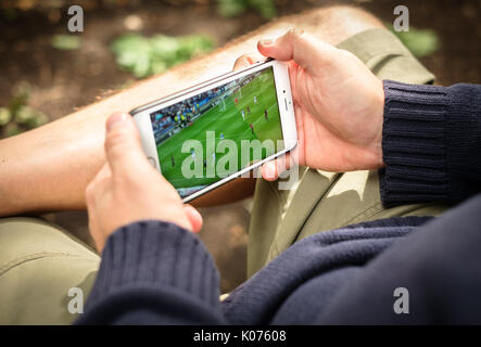 Homme qui regarde un match de football en streaming sur smartphone en zone rurale Banque D'Images