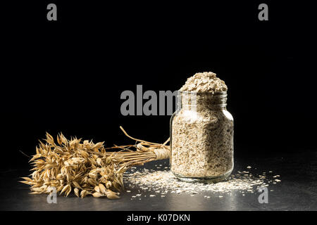 Bouquet d'avoine et flocons dans l'assaisonnement jar, isolé sur fond noir. bouquet, grain de l'avoine d'or sur la table en bois sombre d'épillets, pouvez rempli de séché Banque D'Images