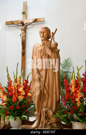 Statue en bois sculpté de Saint Roch avec peste bubo sur cuisse et chien avec du pain qui l'a sauvé dans l'église catholique sanctuaire avec crucifix Banque D'Images