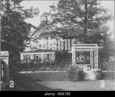 Photographie d'un Roland Park Home à Baltimore avec un beau jardin, la maison faite de briques détaillées avec de grandes fenêtres, la chambre trois étages entre deux grands conifères, United States, 1920. Cette image est tirée d'une série sur la construction et la vente de maisons dans le quartier Roland Park/Guilford de Baltimore, a streetcar suburb et l'une des premières communautés planifiées aux États-Unis. Banque D'Images