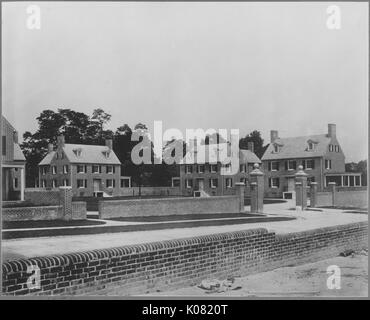 Photographie d'une brique de trois étages Roland Park Homes à Baltimore, entouré de clôtures de brique et brique posts, chaque chambre à tout à fait semblable à l'autre avec deux grandes cheminées et fenêtres de verre simple et un grand porche, United States, 1920. Cette image est tirée d'une série sur la construction et la vente de maisons dans le quartier Roland Park/Guilford de Baltimore, a streetcar suburb et l'une des premières communautés planifiées aux États-Unis. Banque D'Images