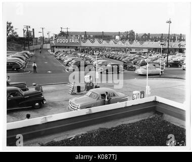 Vue d'une station d'essence avec pompes connectées à des voitures, derrière la station d'essence est un panier-parking pour le Salon de l'alimentation magasin, derrière le salon de l'alimentation store sont en rangée, Baltimore, Maryland, 1951. Banque D'Images