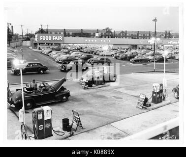 Vue d'une station d'essence avec deux des quatre pompes connectées à des voitures, derrière la station d'essence est un panier-parking pour le Salon de l'alimentation magasin, derrière le salon de l'alimentation store sont en rangée, Baltimore, Maryland, 1951. Banque D'Images