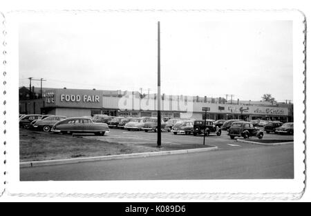 Photographie de l'aire de stationnement pour le centre commercial Northwood, montrant les voitures et les immeubles commerciaux, tels que l'Alimentation juste avec un 'ouverture bientôt !' dans la fenêtre, Baltimore, Maryland, 1951. Banque D'Images