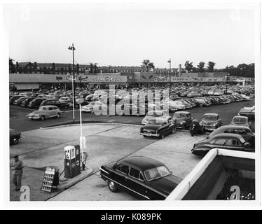 Photographie de l'aire de stationnement pour le centre commercial Northwood à Baltimore, Maryland, montrant de nombreuses voitures et bâtiments commerciaux tels que l'Acme Markets, S S Kresge Company, et le théâtre de Northwood, avec des immeubles d'habitation et arbres en arrière-plan, Baltimore, Maryland, le 14 juin 1951. Banque D'Images